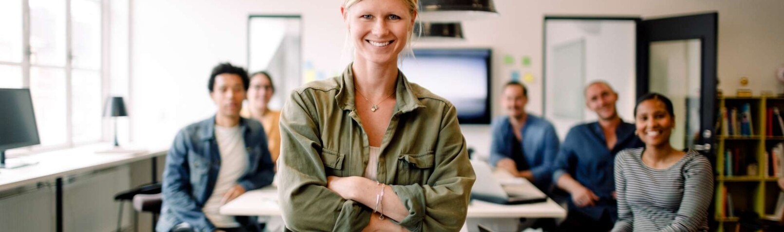 Eine Frau steht lächelnd vor einem Tisch, dahinter sitzt ihr Team