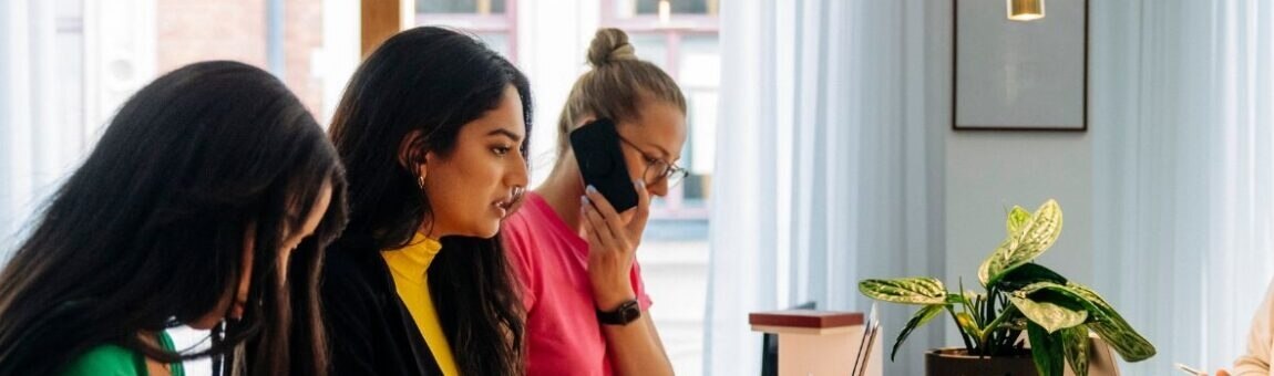 Eine Gruppe von Frauen arbeitet zusammen, während sie an einem Tisch im Büro sitzen