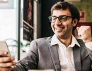 Ein Geschäftsmann im Anzug sitzt im Restaurant, schaut erfreut auf sein Handy und ballt die Faust.