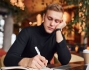 Junger Mann am Schreibtisch mit Laptop und Notizbuch