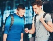 Zwei junge Menschen mit Reisetaschen schauen auf ein Smartphone