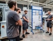 Eine Gruppe junger Männer steht in einer Werkstatt und bespricht sich.