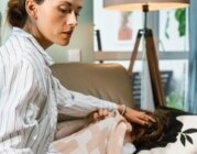 Mutter betreut ihr krankes Kind, das zugedeckt auf der Couch liegt.