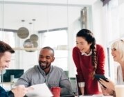 Mitarbeiter*innen lachend zusammen im modernen Büro am Schreibtisch.