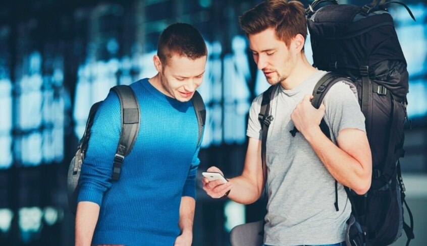 Zwei junge Menschen mit Reisetaschen schauen auf ein Smartphone