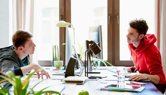 Zwei Männer sitzen sich am Bürotisch gegenüber und besprechen sich.