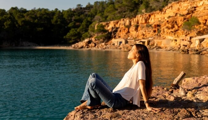 Junge Frau sitzt an der Küste am Meer und entspannt in der Sonne.